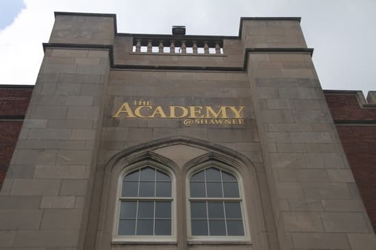 Stone facade of The Academy @ Shawnee, gold lettering above two arched Gothic windows, seen from below against an overcast sky